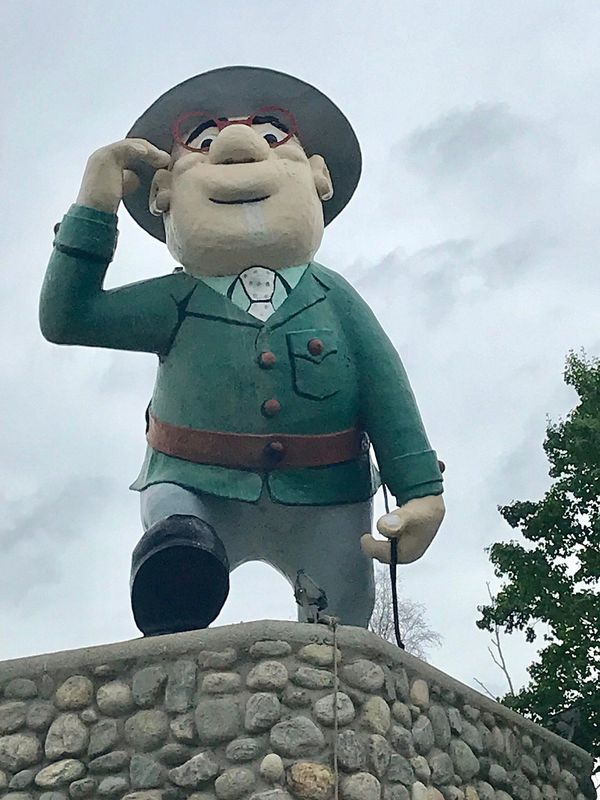 Large statue of a man with glasses and a green jacket on a stone pedestal.