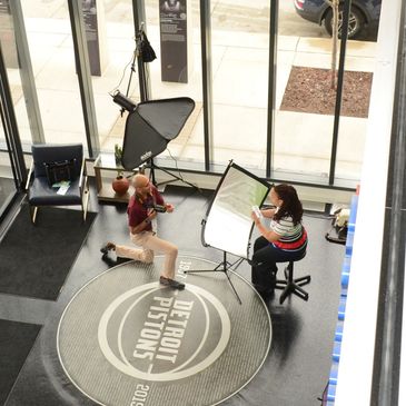 Photographer taking a portrait of a seated woman in a studio with Detroit Pistons logo.