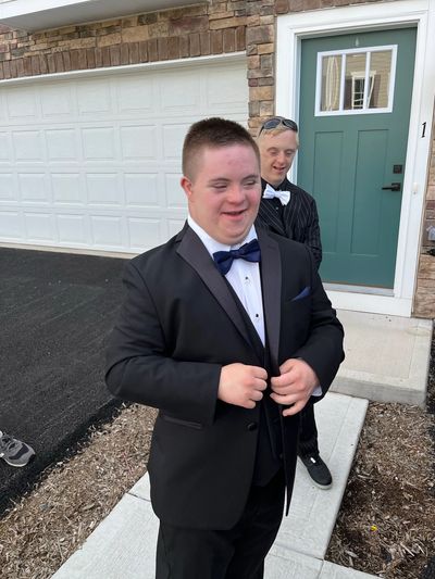 Two young men in tuxedos smiling outside a house.