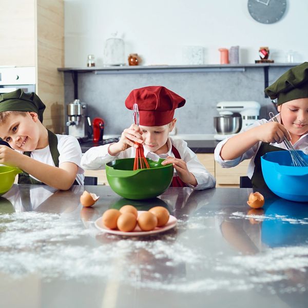 Three children in chef hats mixing ingredients in bowls on a kitchen counter.
