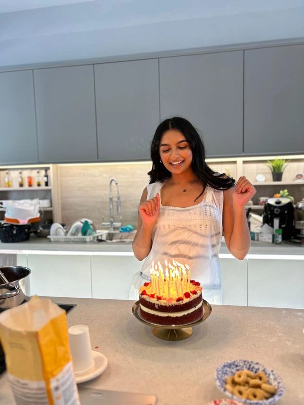 A woman joyfully prepares to blow out candles on a birthday cake in a modern kitchen.