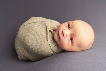 Newborn baby wrapped in a beige blanket lying on a gray surface.
