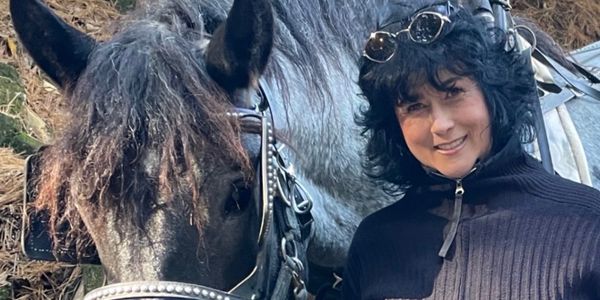 Woman smiling beside a gray horse in outdoor setting.
