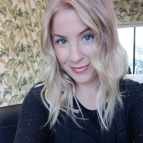 Smiling young woman with blonde wavy hair and blue eyes indoors.
