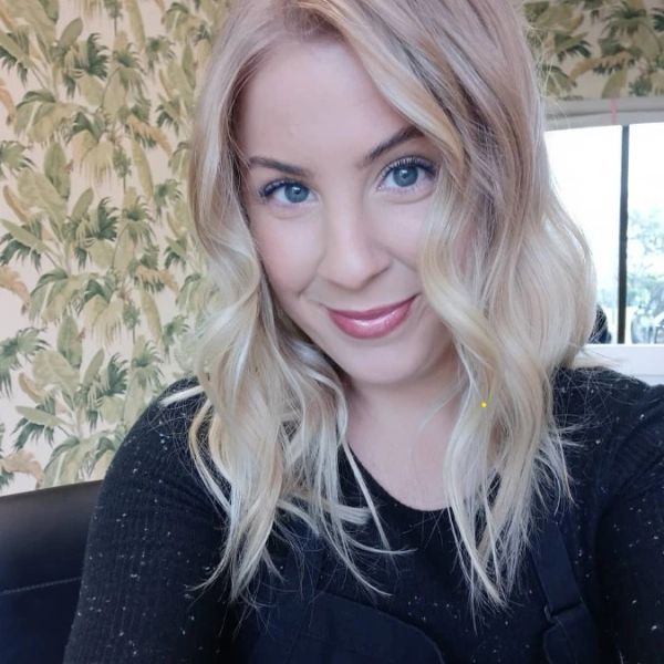 Smiling young woman with blonde wavy hair and blue eyes indoors.