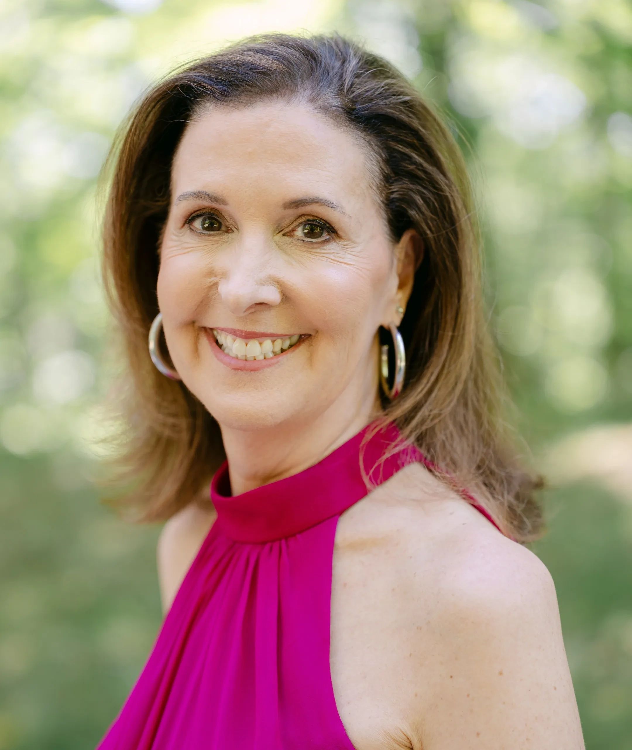 Smiling woman in a magenta halter top with hoop earrings.