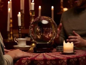 A crystal ball on a table with candles and people around it.