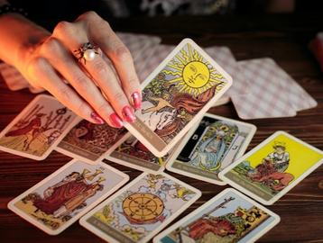 Hand holding The Sun tarot card over a spread of tarot cards.