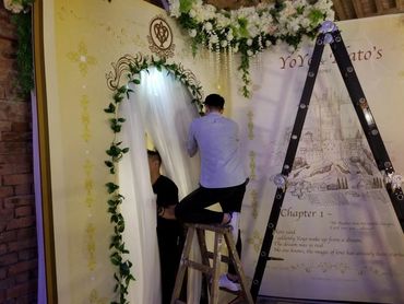 Two men set up a decorated arch and backdrop for an event.
