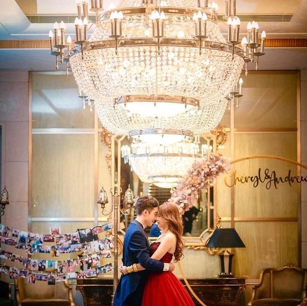 Couple in elegant attire embracing under a grand chandelier.