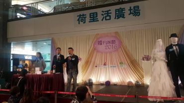 A couple stands on stage at a 2016 wedding-themed event with mannequins in wedding attire.
