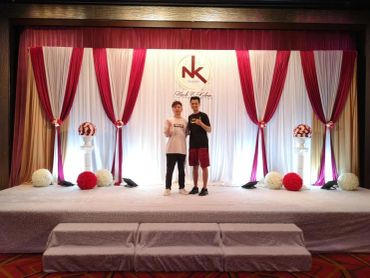 Two people stand on a decorated stage with red and white drapes.