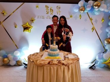 Family celebrating a child's birthday with a decorated cake and balloons.