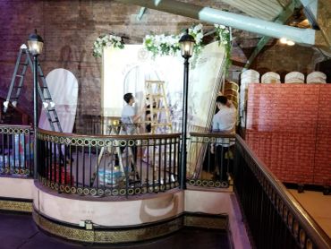 Two workers setting up a decorated backdrop with ladders indoors.