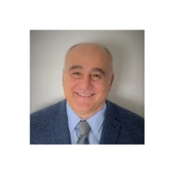 Portrait of a smiling man in a suit and tie against a neutral background.
