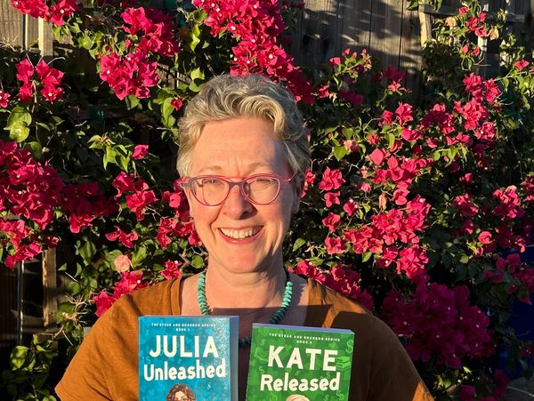 Smiling woman holding two books with vibrant flowering background.
