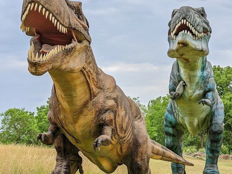 Two large dinosaur statues with open mouths in a grassy field.