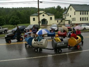 People riding a colorful barrel train on a rainy street.