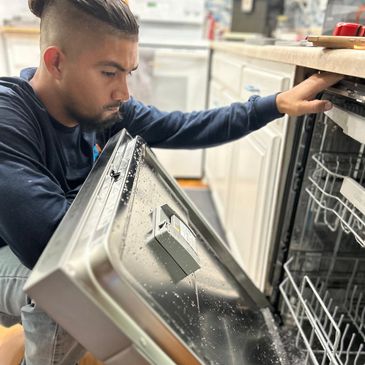 Man fixing a dishwasher with the door open in a kitchen.
