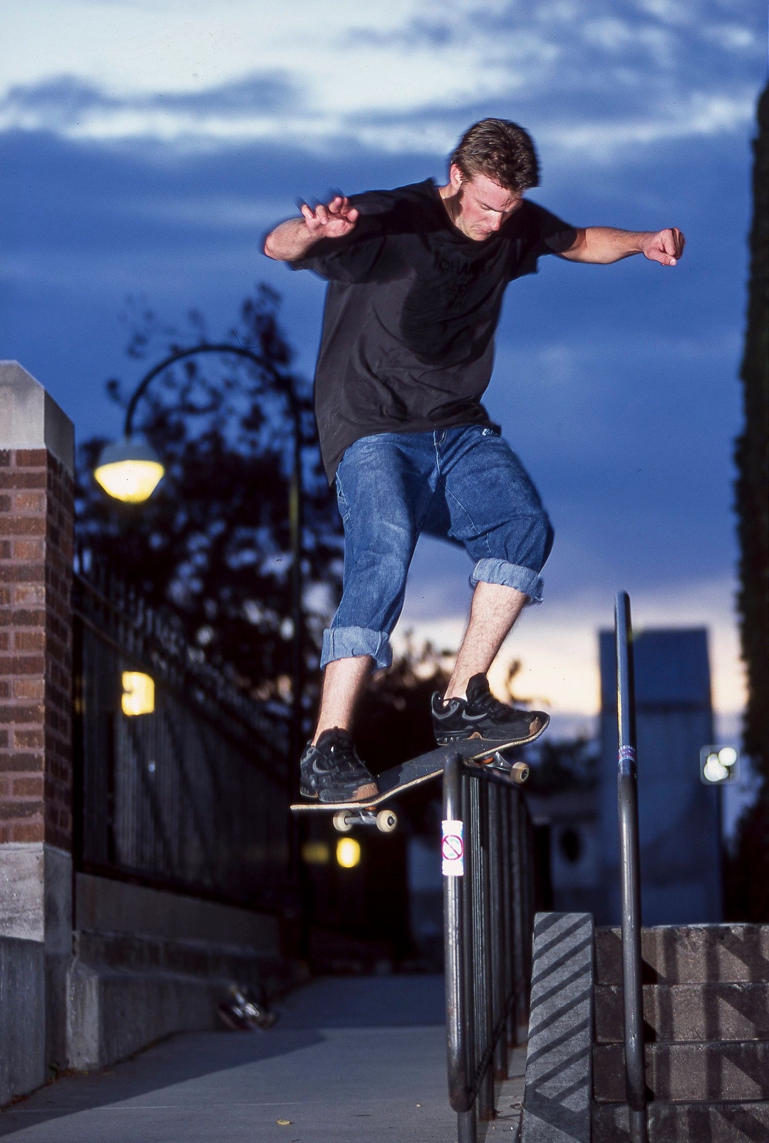 Skateboarder grinding a rail at dusk in casual attire.