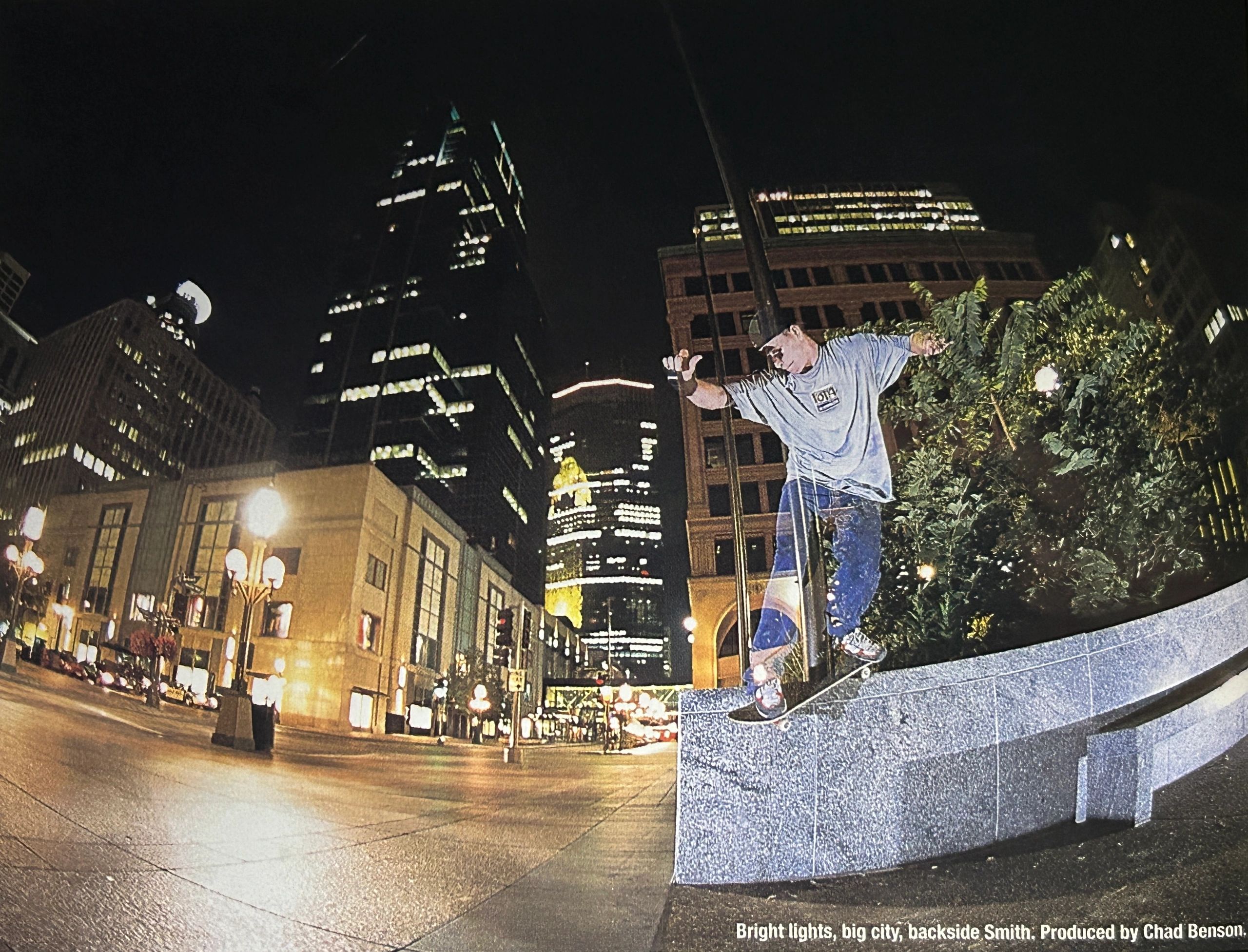 Skateboarder performing a backside Smith grind on a ledge in a city at night.