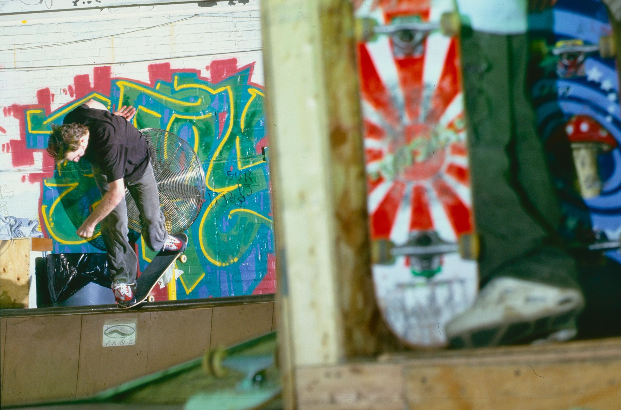 Skateboarder performing a trick in front of colorful graffiti indoors.