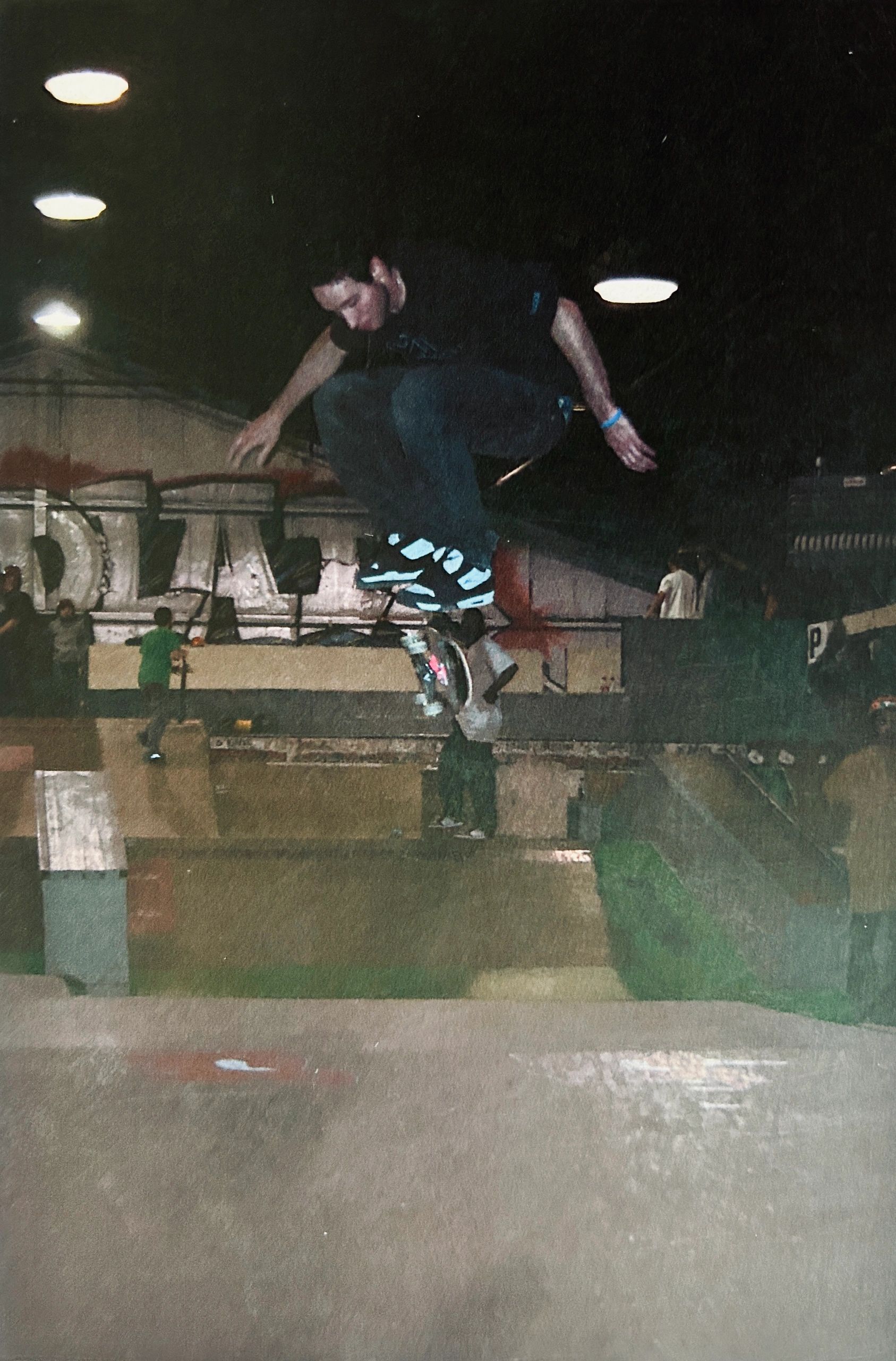 Skateboarder performing a trick at night in a skatepark with graffiti in the background.