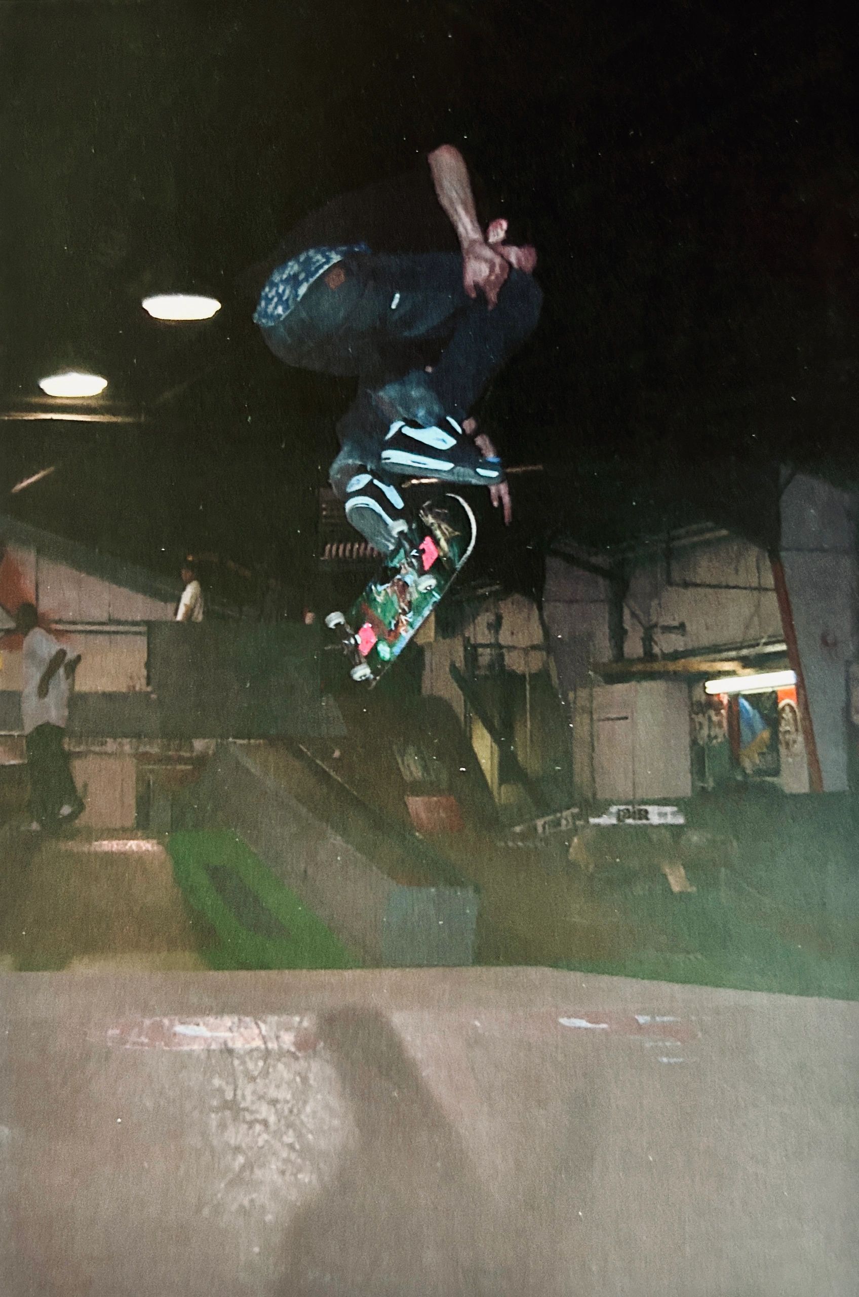 Skateboarder performing a high trick at night in a skatepark.