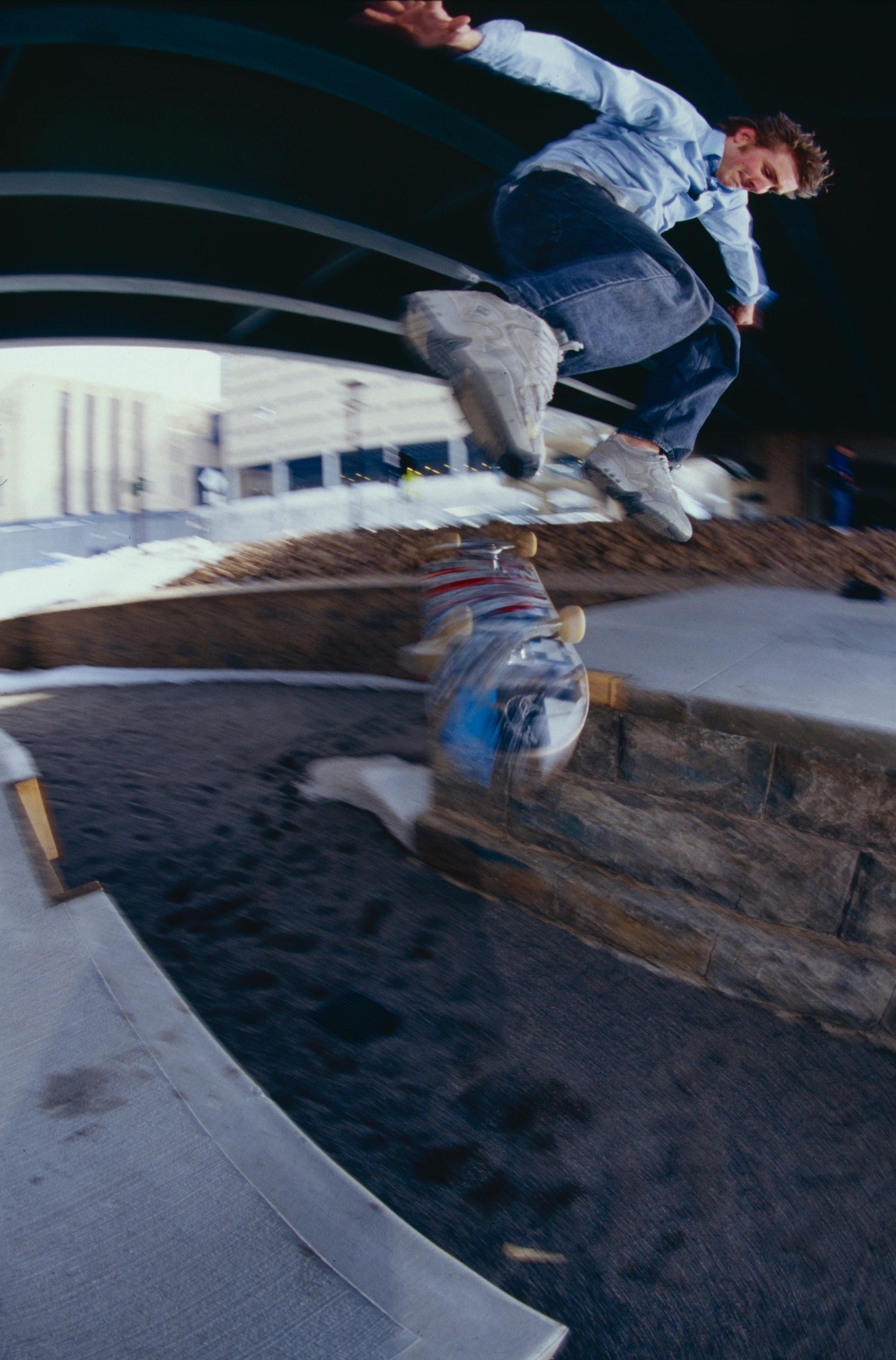 Skateboarder performing a trick mid-air under a bridge in an urban setting.