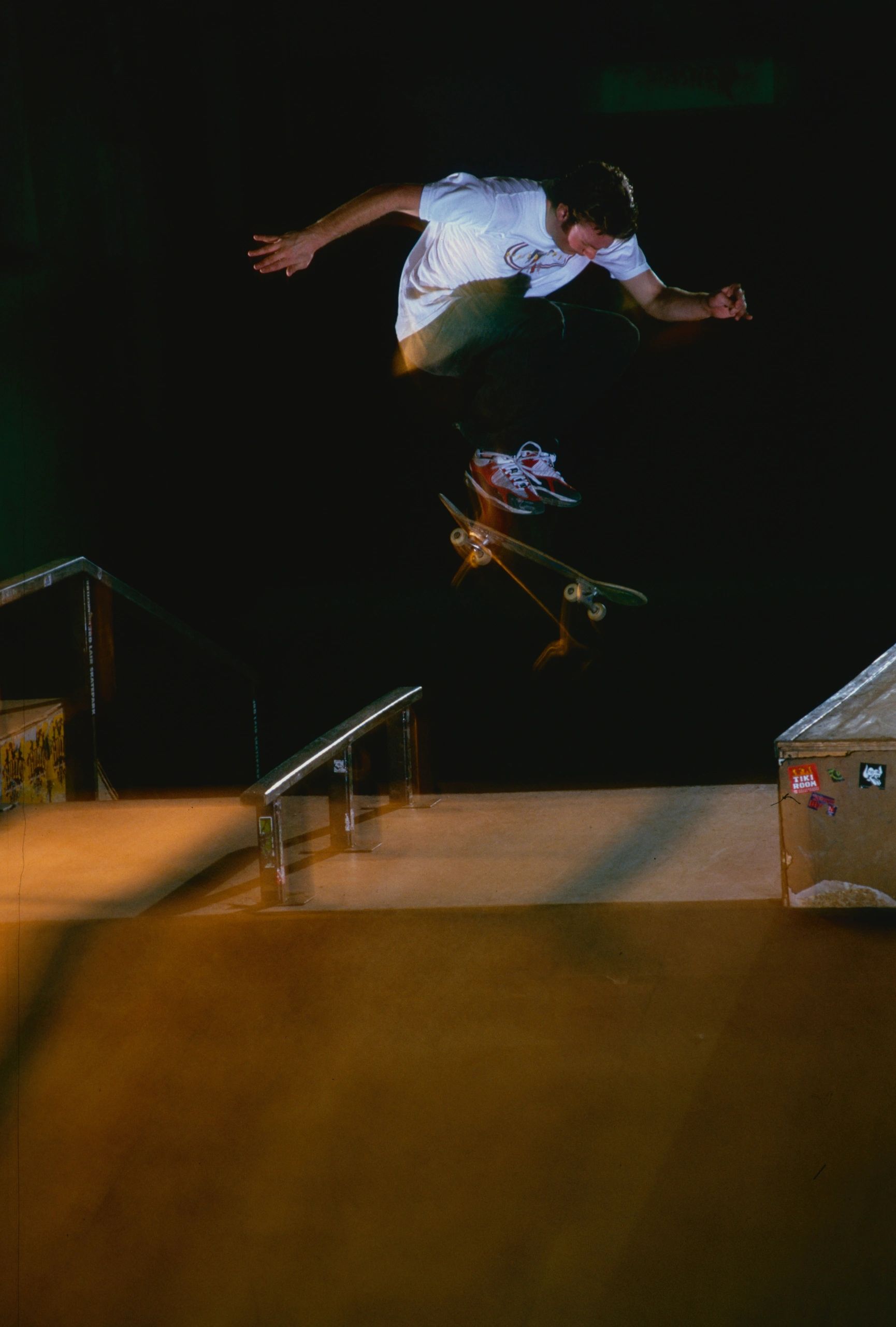 Skateboarder performing a trick mid-air at a skatepark under dramatic lighting.