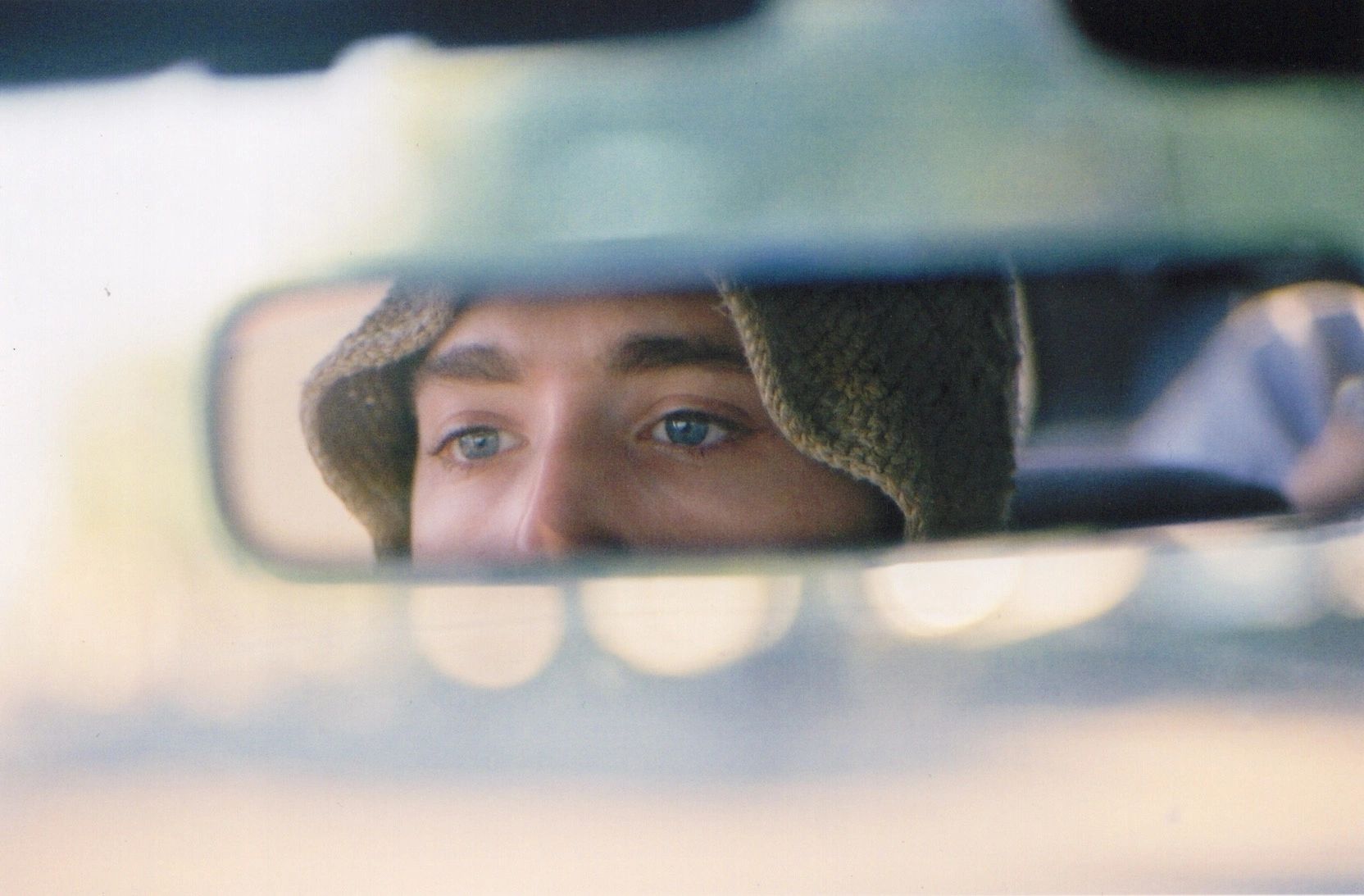 Reflection of a person wearing a knitted hat in a car's rearview mirror.