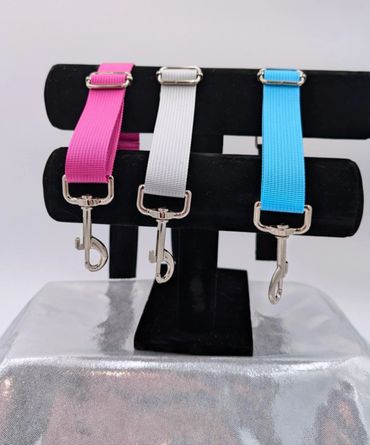 Three colorful pet leashes in pink, white, and blue displayed on a black stand.