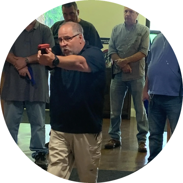 Man aiming a training gun indoors with others observing.