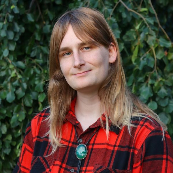 Photo of Cáit, a woman with long blonde hair, wearing a red flannel and bolo tie.