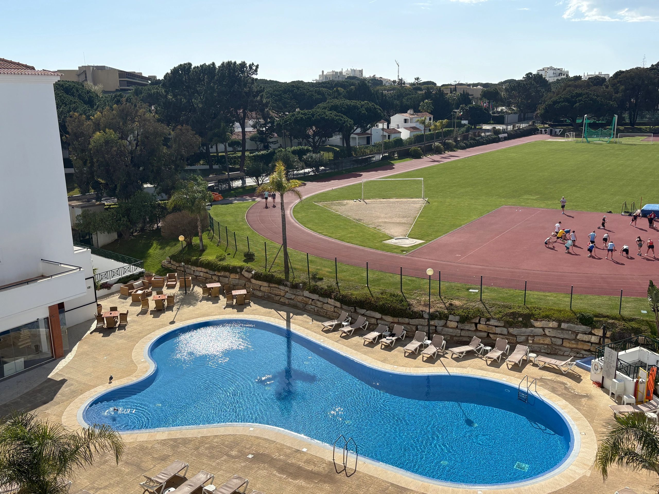Outdoor pool and sports field with people.