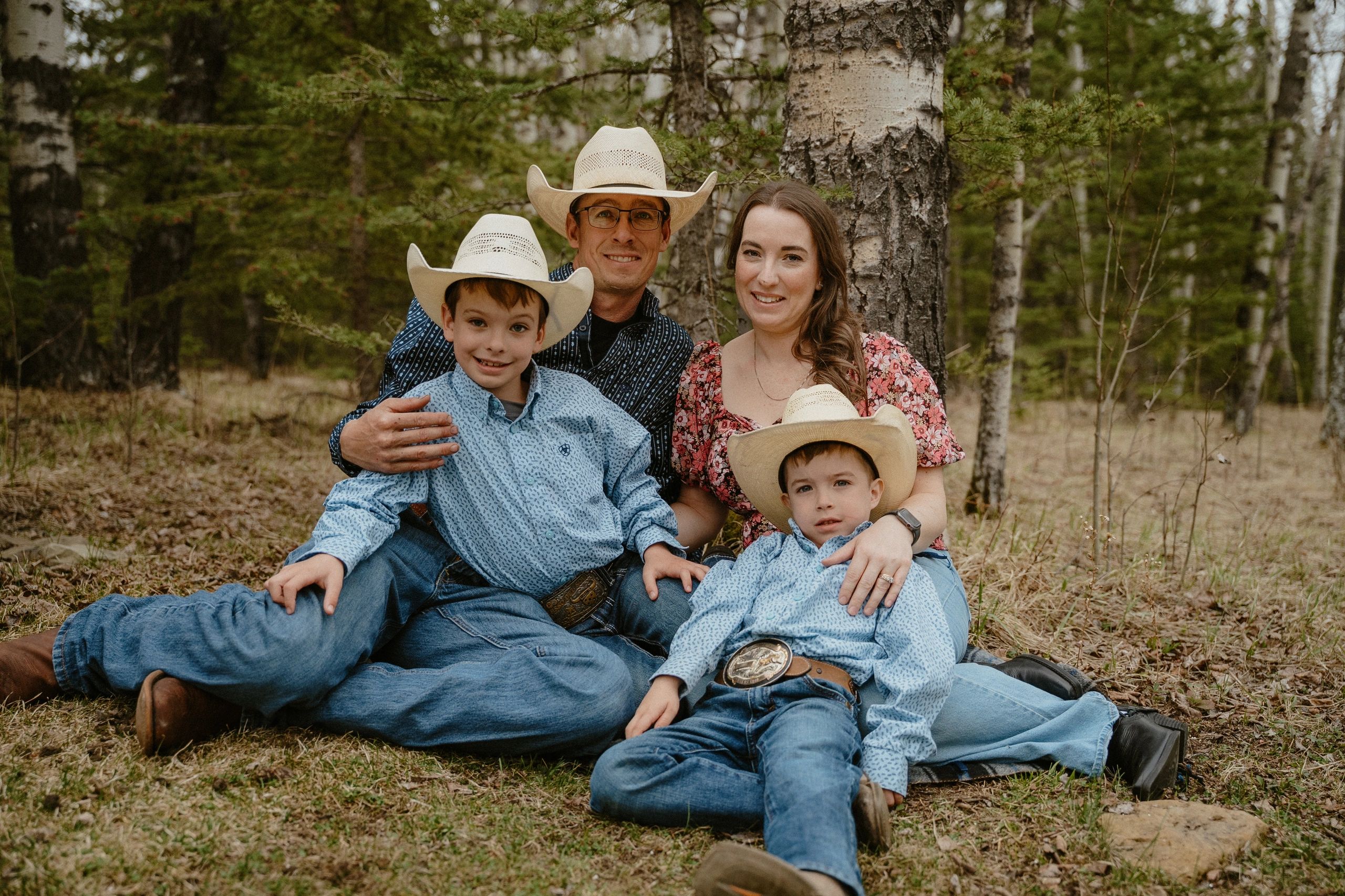 Smiling family of four in cowboy hats sitting in a forest.