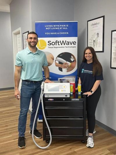 Two people standing beside SoftWave tissue regeneration machine in a clinic.