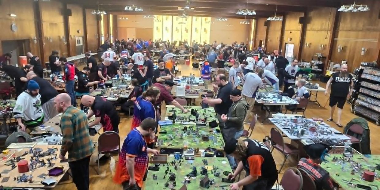 A large group of people playing tabletop games in a spacious hall.
