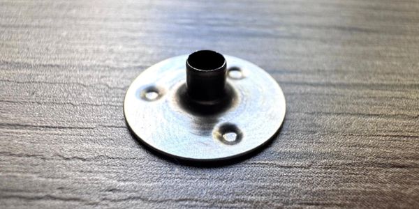 A small metal flange with three screw holes on a textured surface.