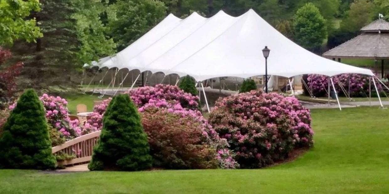 Large white event tent set in a lush garden with pink flowering bushes and green trees.