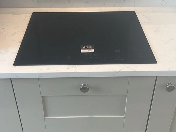 Black AEG induction cooktop on white marble countertop with light gray cabinets.