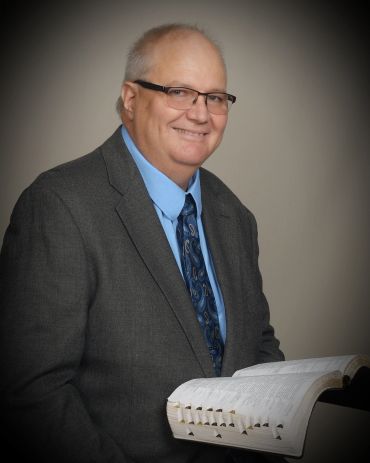 Man in suit holding an open book and smiling.