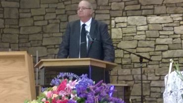 Man speaking at a podium with flowers in front.