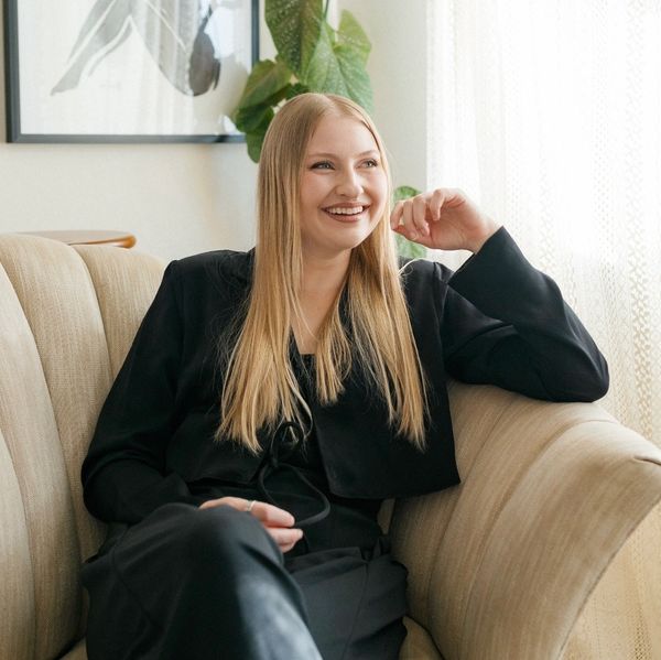 Smiling woman with long blonde hair sitting on a beige couch.