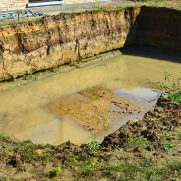 A flooded construction pit with muddy water and exposed soil layers.