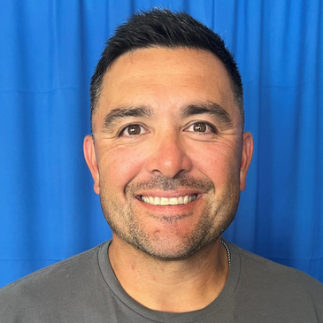 Smiling man with short hair against a blue backdrop.