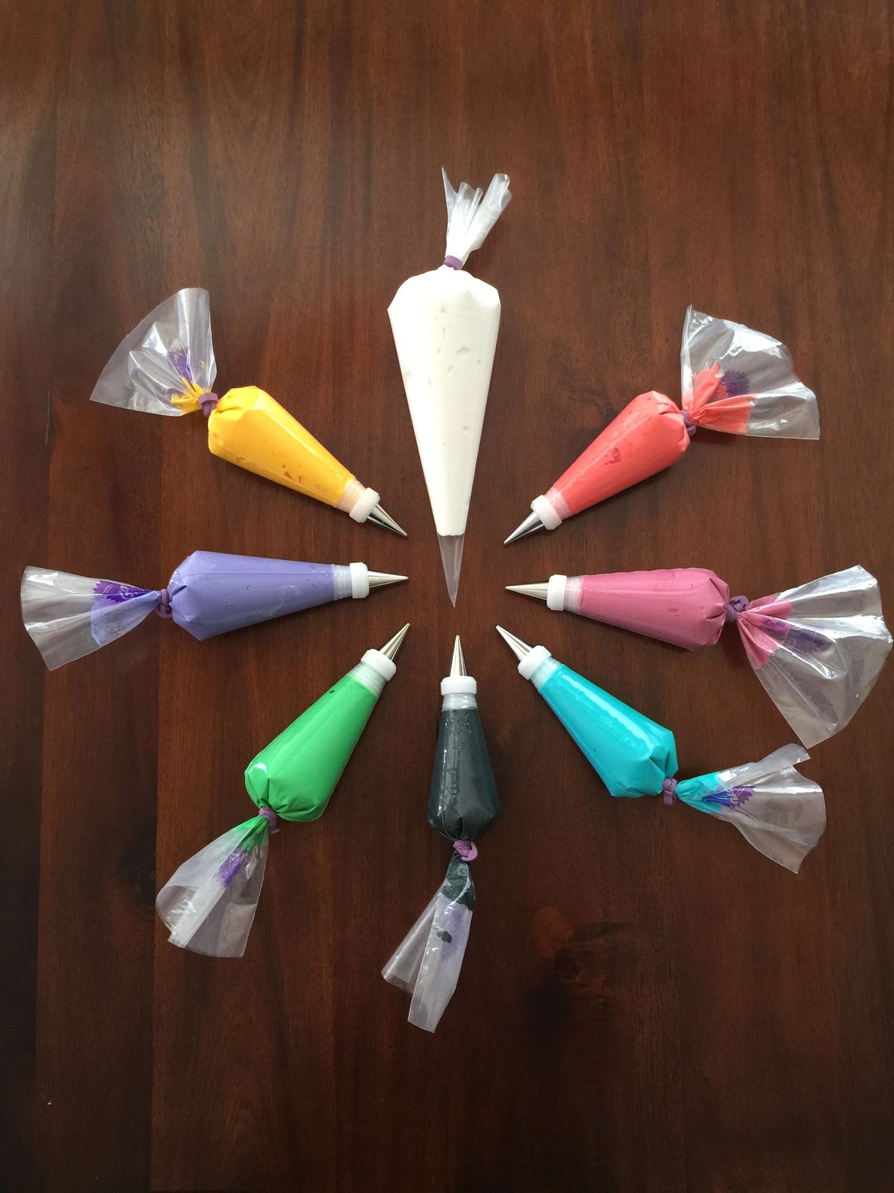 Different colors of royal icing bags with decorating tips in a circle.