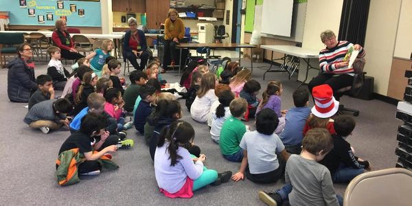 A woman reads a book to a group of children in a classroom.