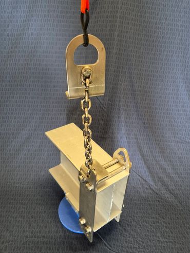 Metal lifting clamp attached to a chain and hook against a textured backdrop.