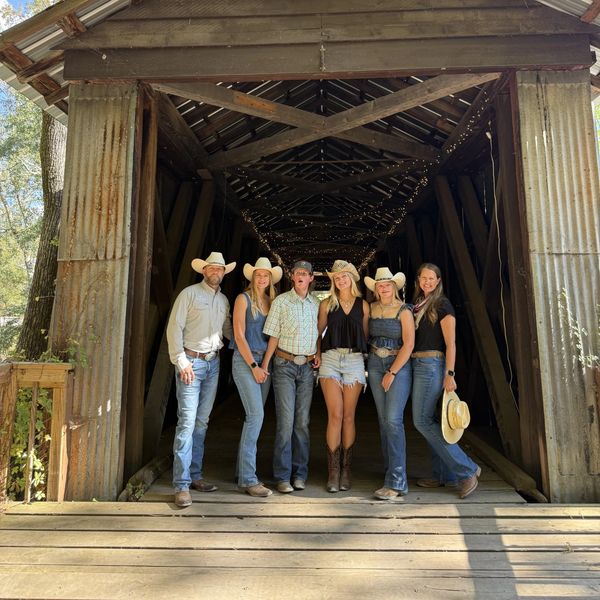 Group of six people in casual western wear standing on a wooden bridge.